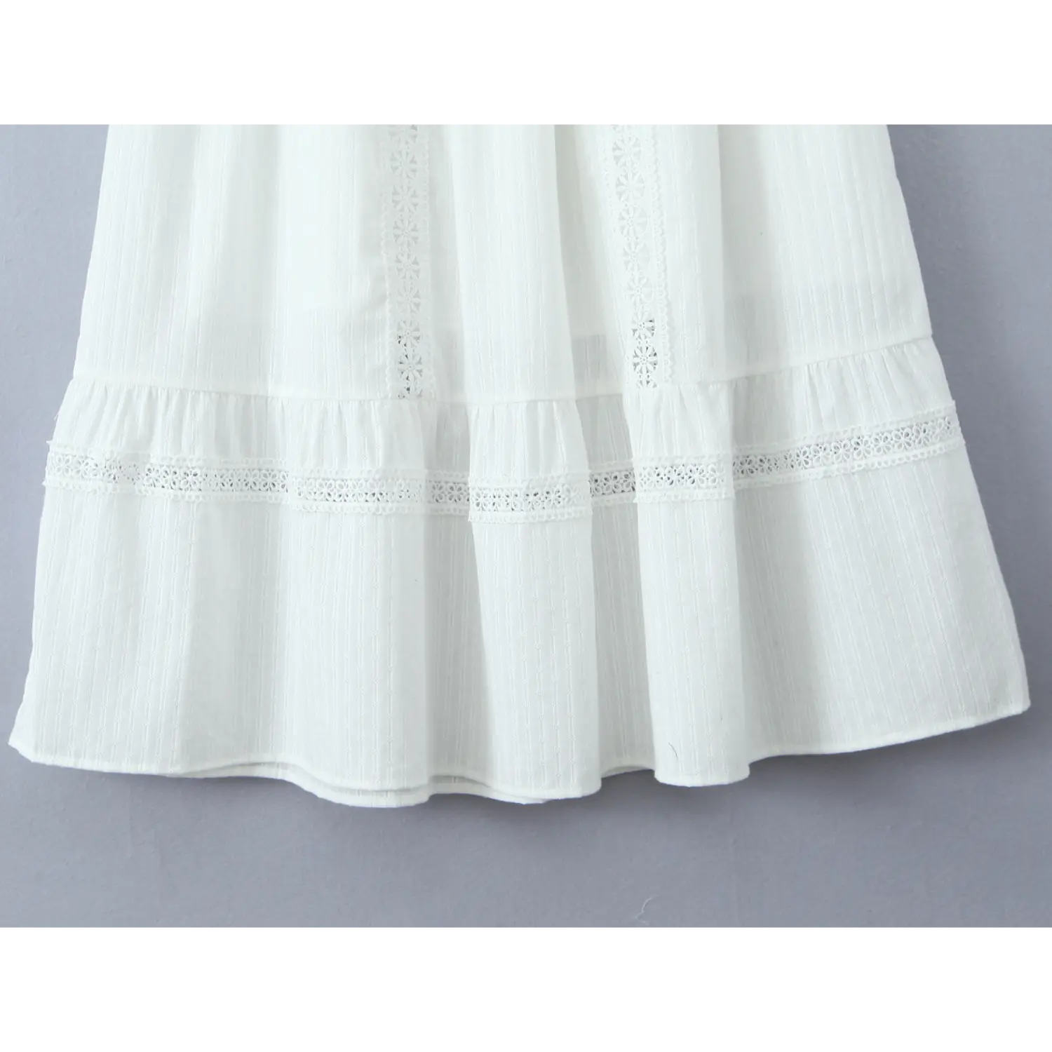 Close-up of the hem of a white tiered maxi skirt, featuring eyelet lace trim and textured fabric