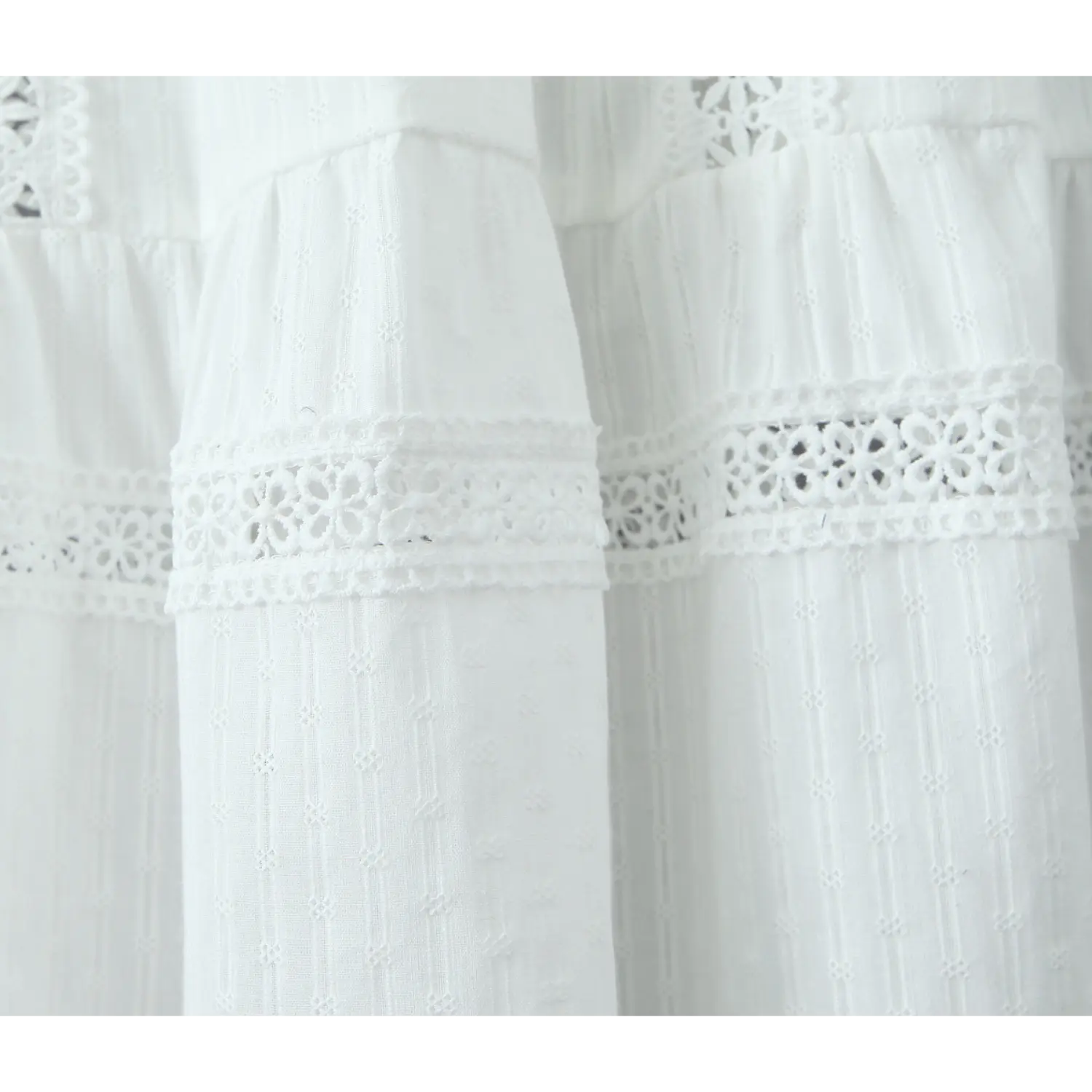 Close-up of the tiered construction on a white maxi skirt, showing horizontal eyelet lace trim between tiers