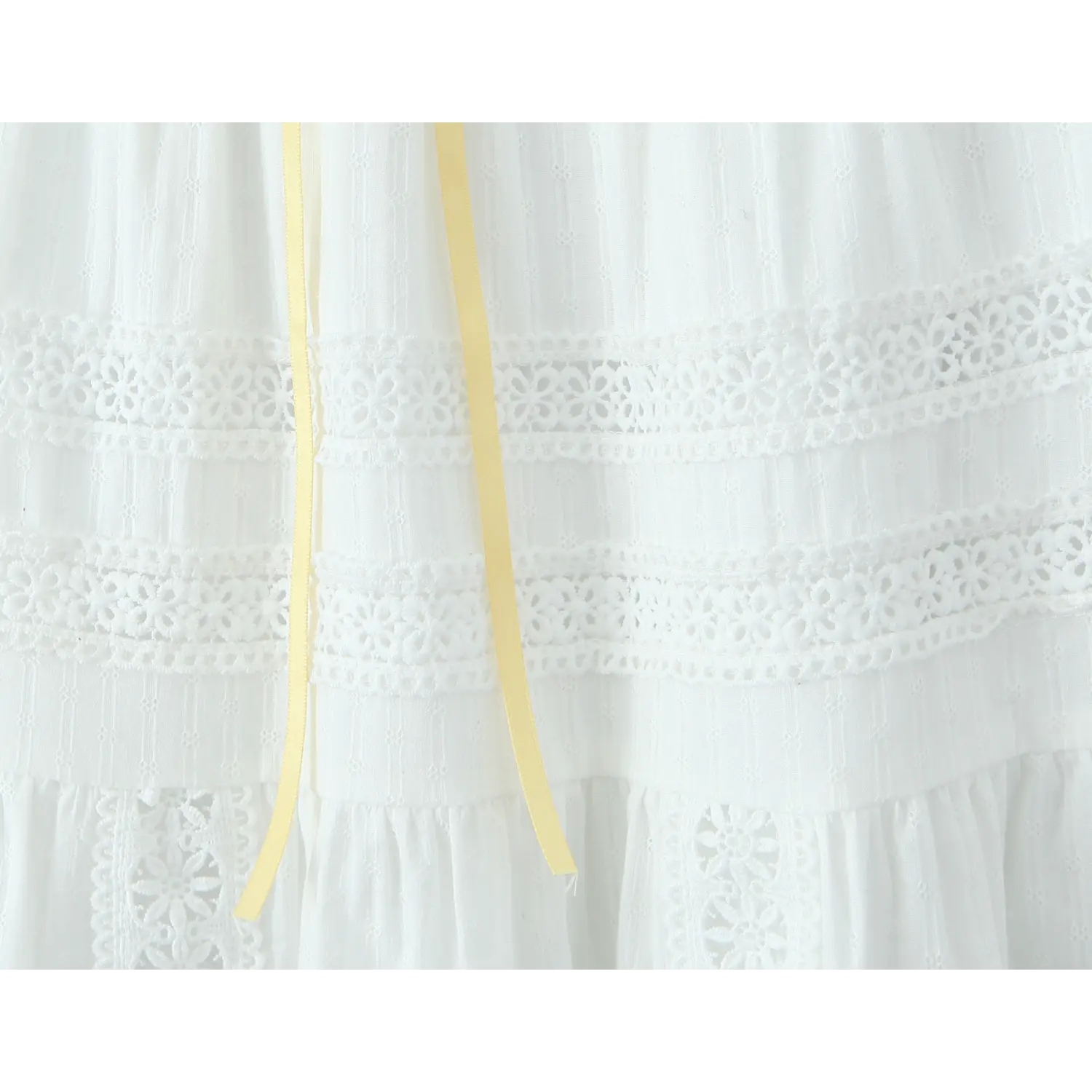 Close-up of the waistband on a white tiered maxi skirt, showing a yellow ribbon drawstring and double rows of eyelet lace