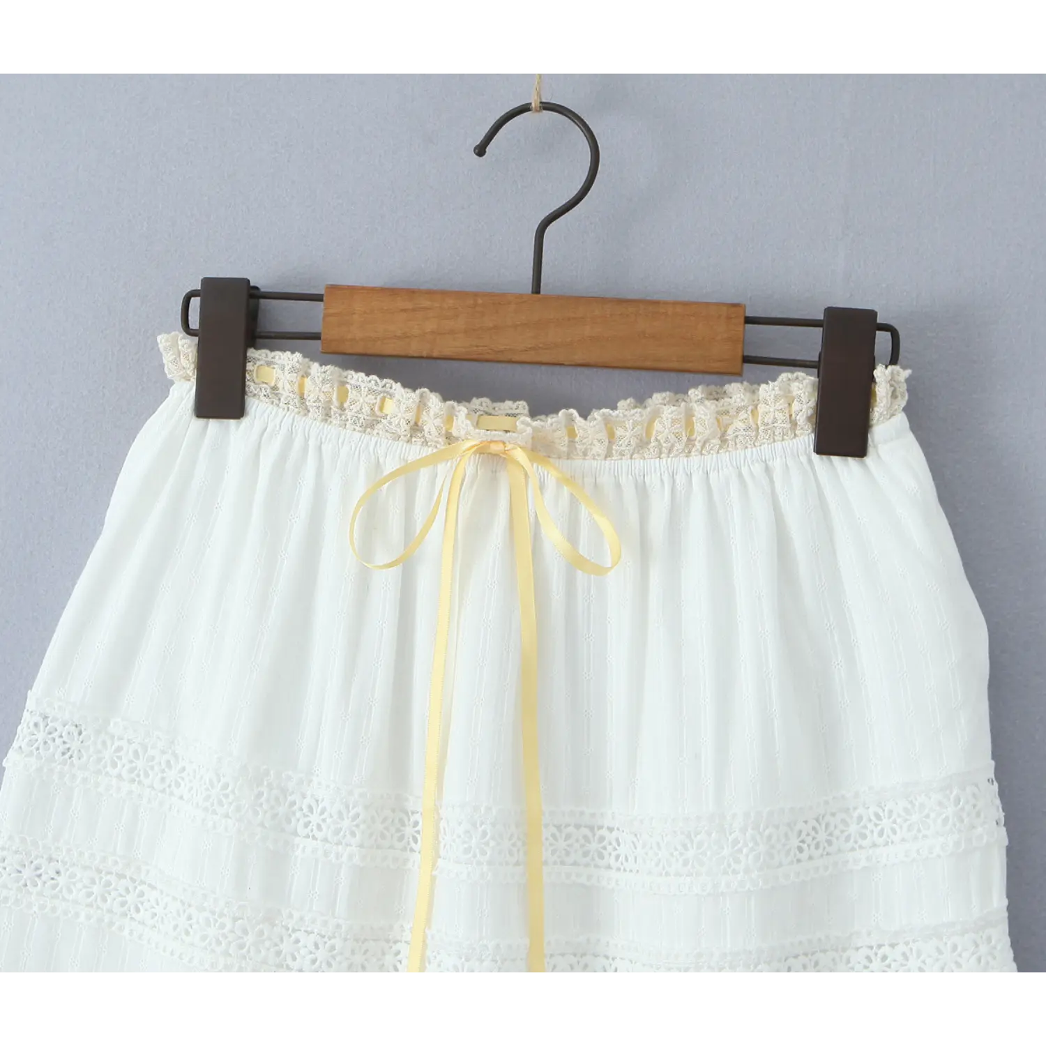 Close-up of the elasticated waistband on a white tiered maxi skirt, featuring ruffled lace trim and a yellow ribbon bow