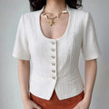 Model wearing white u‑neck textured cropped short sleeve jacket with silver spiral buttons and patch pockets, fitted tailored silhouette, grey background