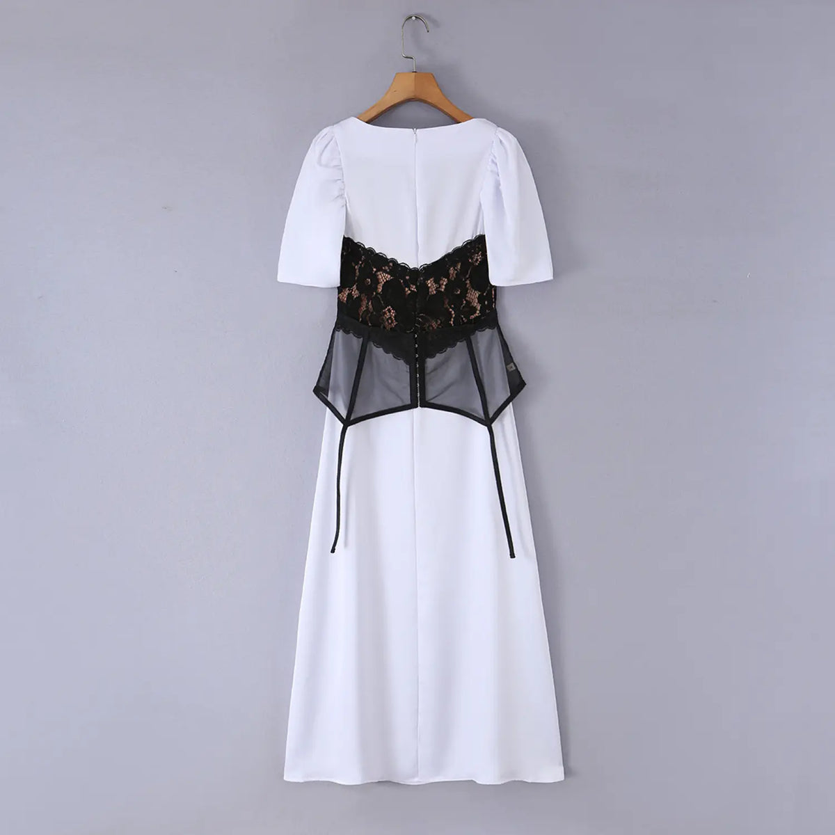 White maxi dress with black lace peplum overlay hanging on wooden hanger, back view