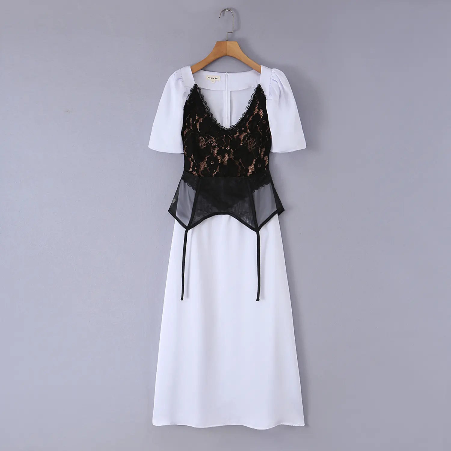 White maxi dress with black lace peplum overlay hanging on wooden hanger, front view