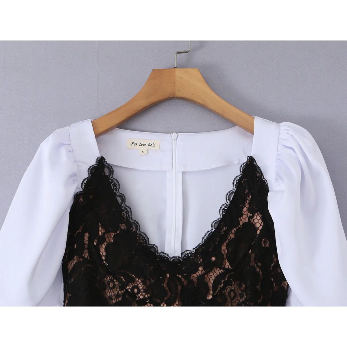 Hanger close‑up of v‑neck, puff shoulder and black lace bust overlay