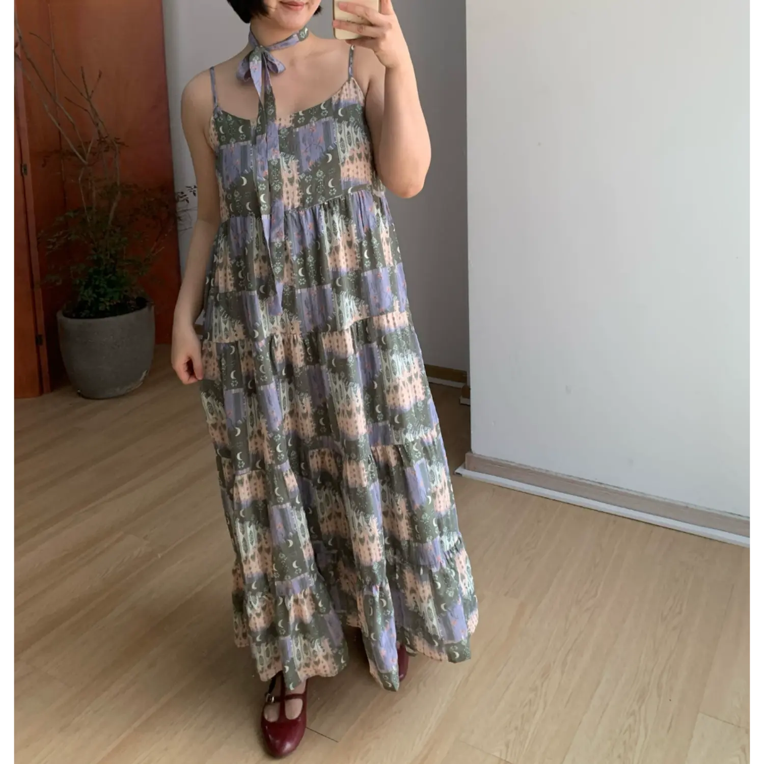 Full spread front indoor mirror shot of ultra-loose multi-tier ruffle cami maxi sundress, retro collage castle & crescent moon print, matching self-fabric neck tie choker, thin adjustable spaghetti straps, extra flowy floor-length tiered skirt, burgundy strap flat shoes, plain white wall & light wood flooring backdrop