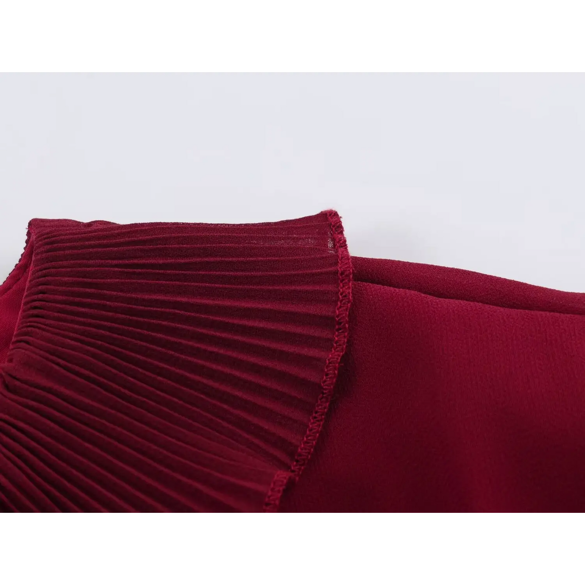 Close-up of wine red fabric showing pleated texture joined with flat fabric by matching stitching