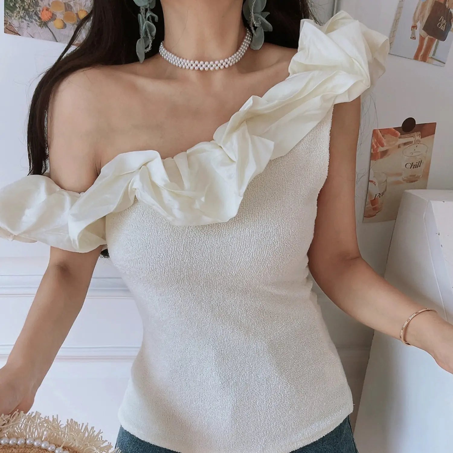 Women cream textured knit one shoulder crop top, spliced chiffon ruffle trim fitted waist, indoor half body model shot with denim jeans