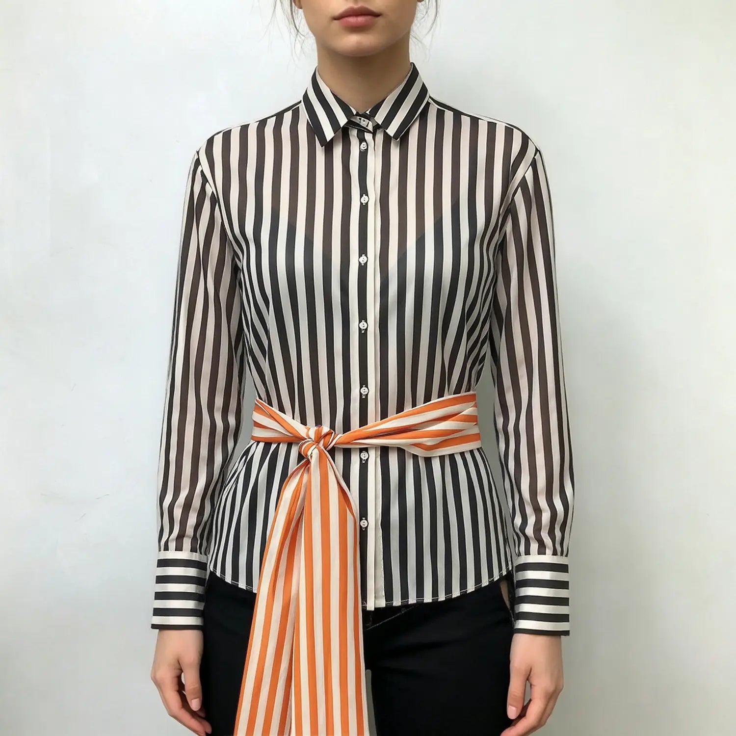 Model front view wearing black‑off‑white vertical stripe long sleeve collared shirt, knotted orange‑white striped waist sash, paired with black pants