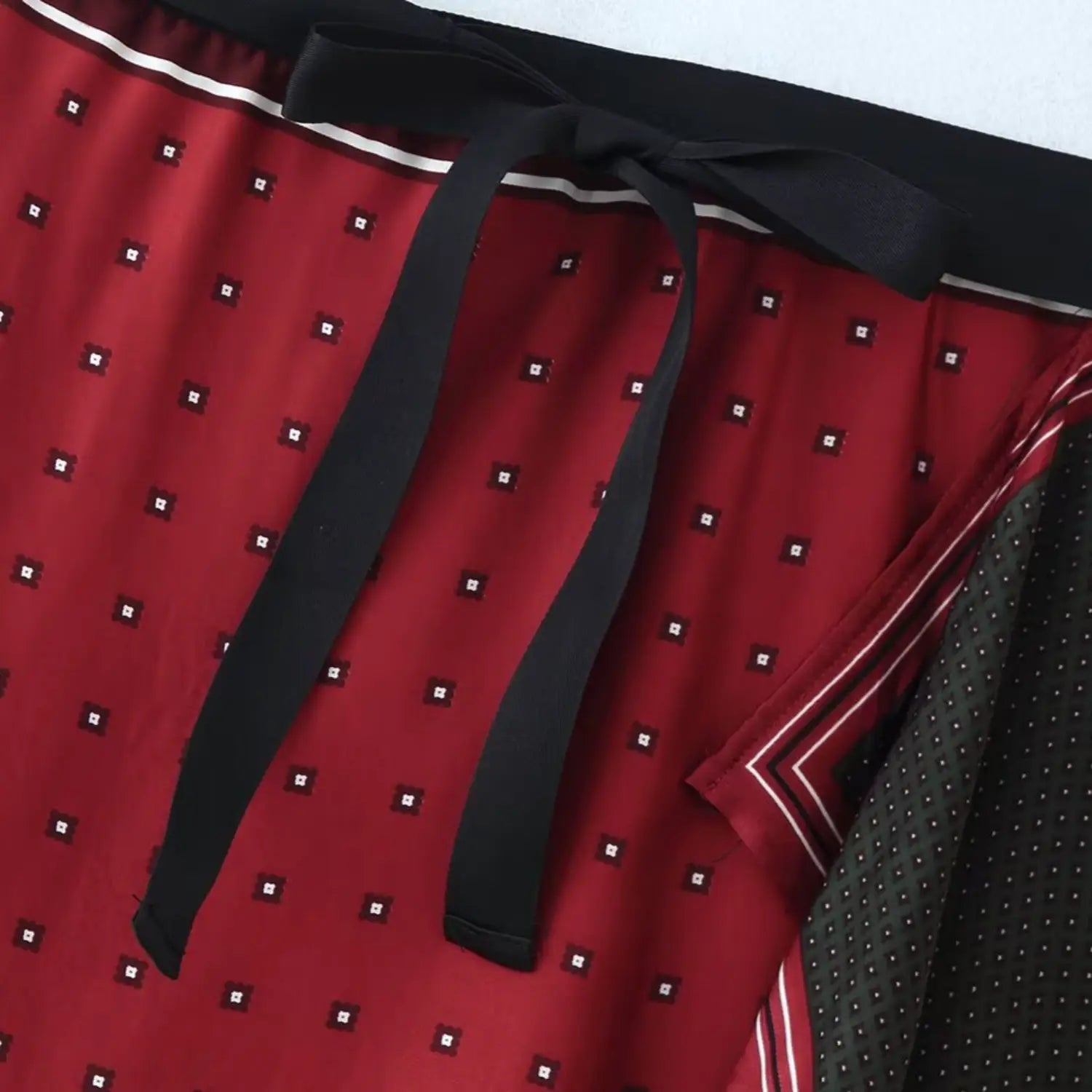 Close-up of wide elastic waistband and long black fabric tie ribbon on red geometric dot outer fabric