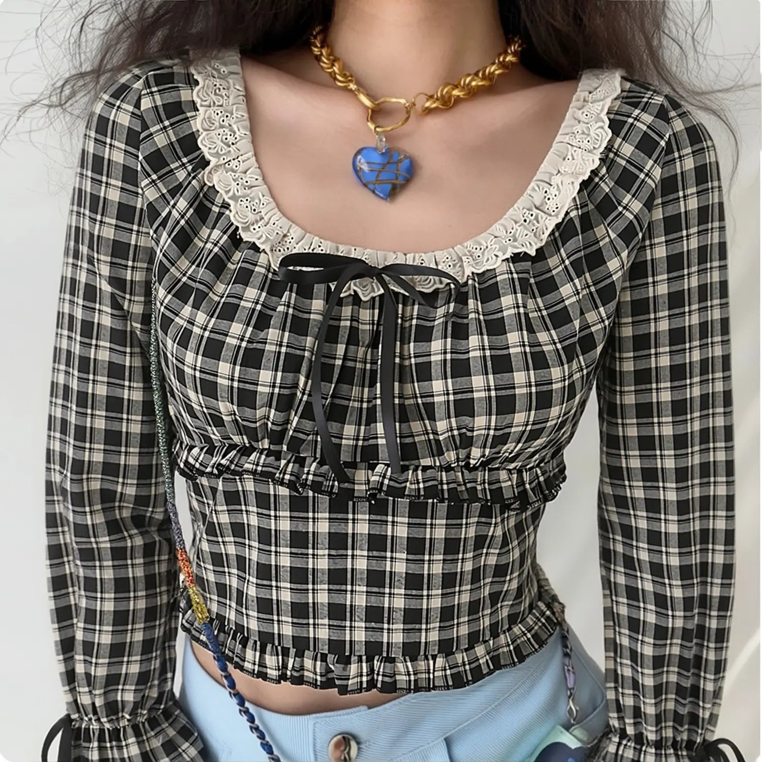 Model wearing vintage black cream check long sleeve cropped blouse, eyelet lace square neck with front satin bow, tiered ruffle waist, flare ribbon cuffs, paired with light blue jeans, sweet casual streetwear outfit