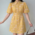 Lifestyle full-body shot of model wearing yellow floral shirt mini dress with puff sleeves, paired with brown crocodile shoulder bag