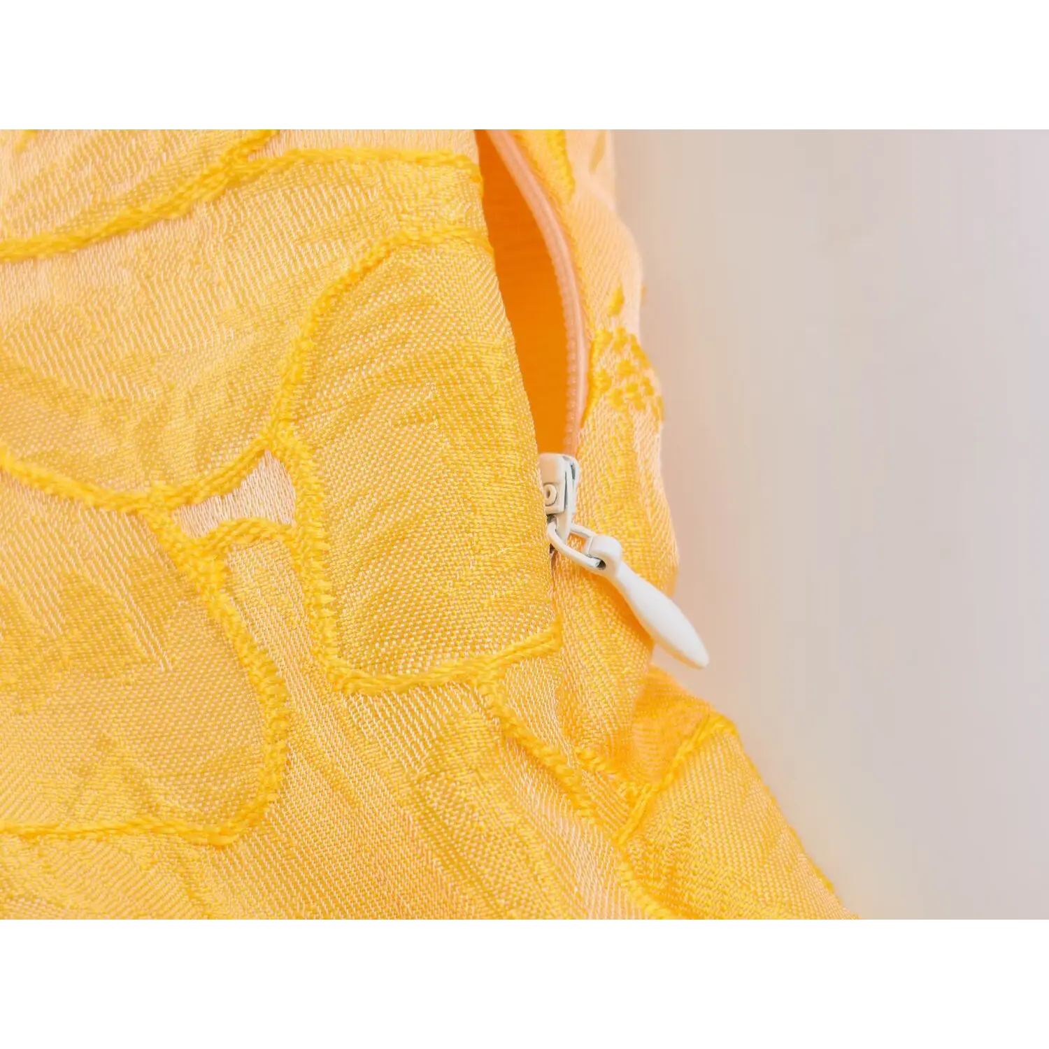 Close-up of invisible side zipper with white fabric pull tab, textured yellow floral fabric