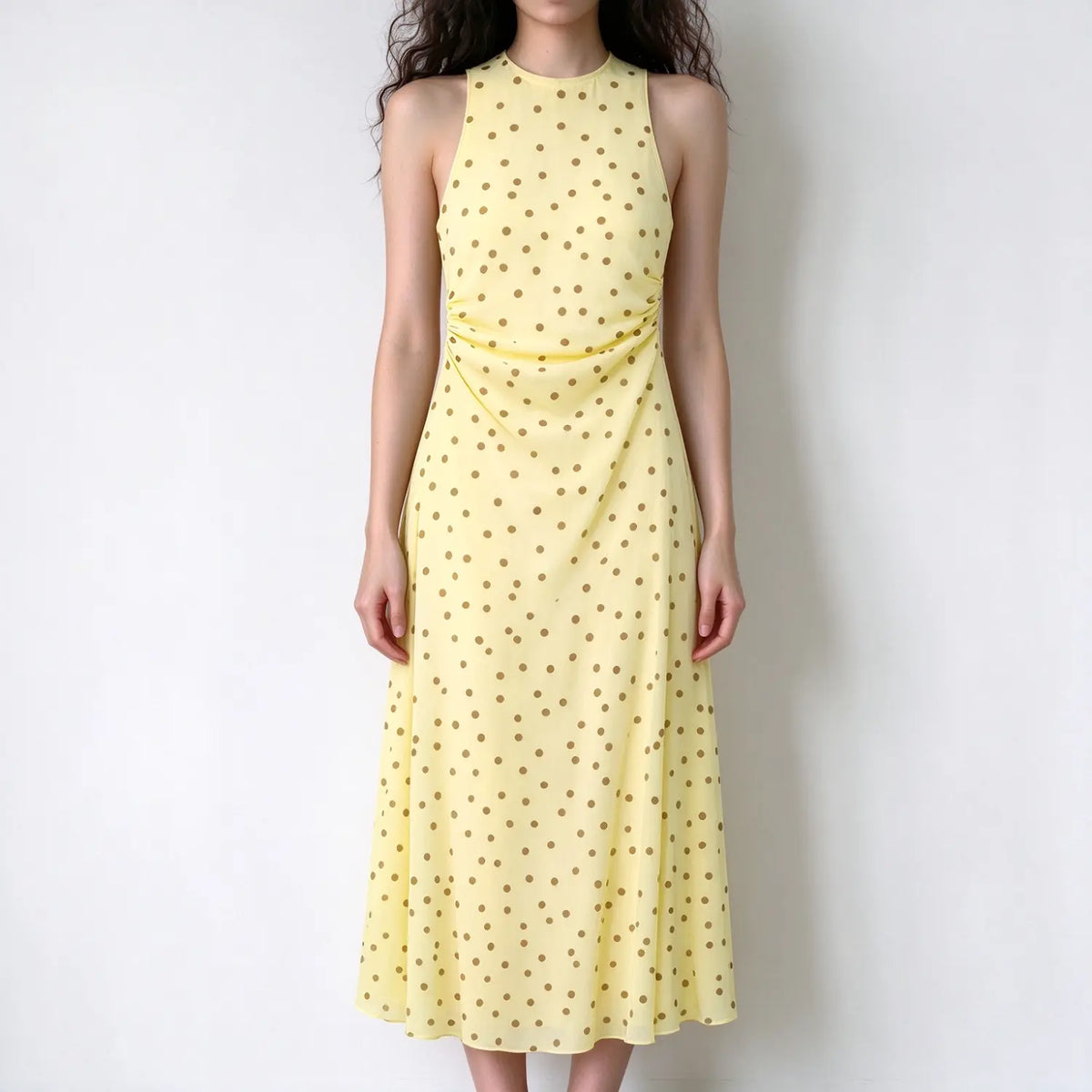 Model wearing yellow brown polka dot sleeveless halter maxi dress, waist ruched detail, soft flowy fabric, plain white backdrop