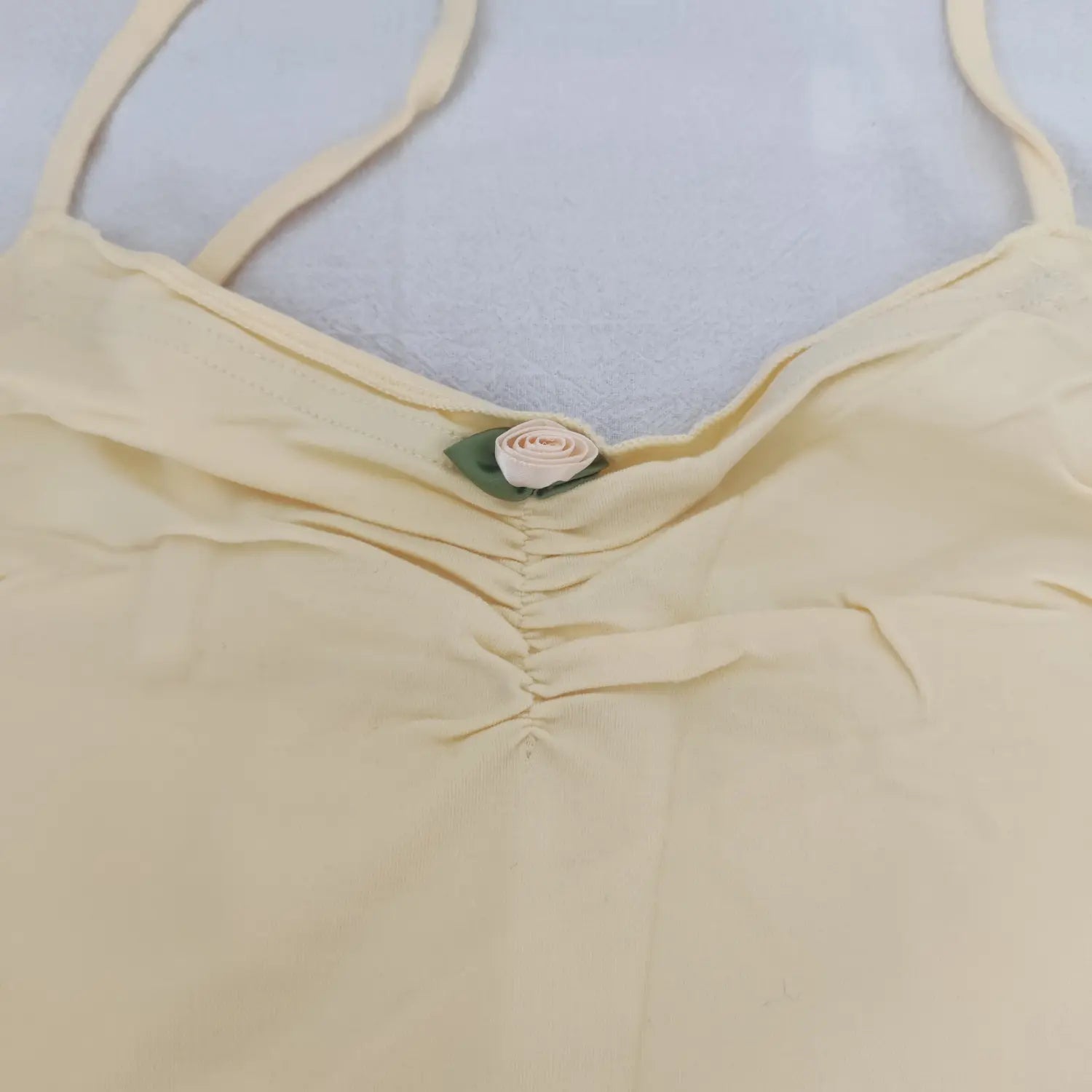 Close-up front bust, ruched design with small rose flower ornament on pale yellow spaghetti strap dress