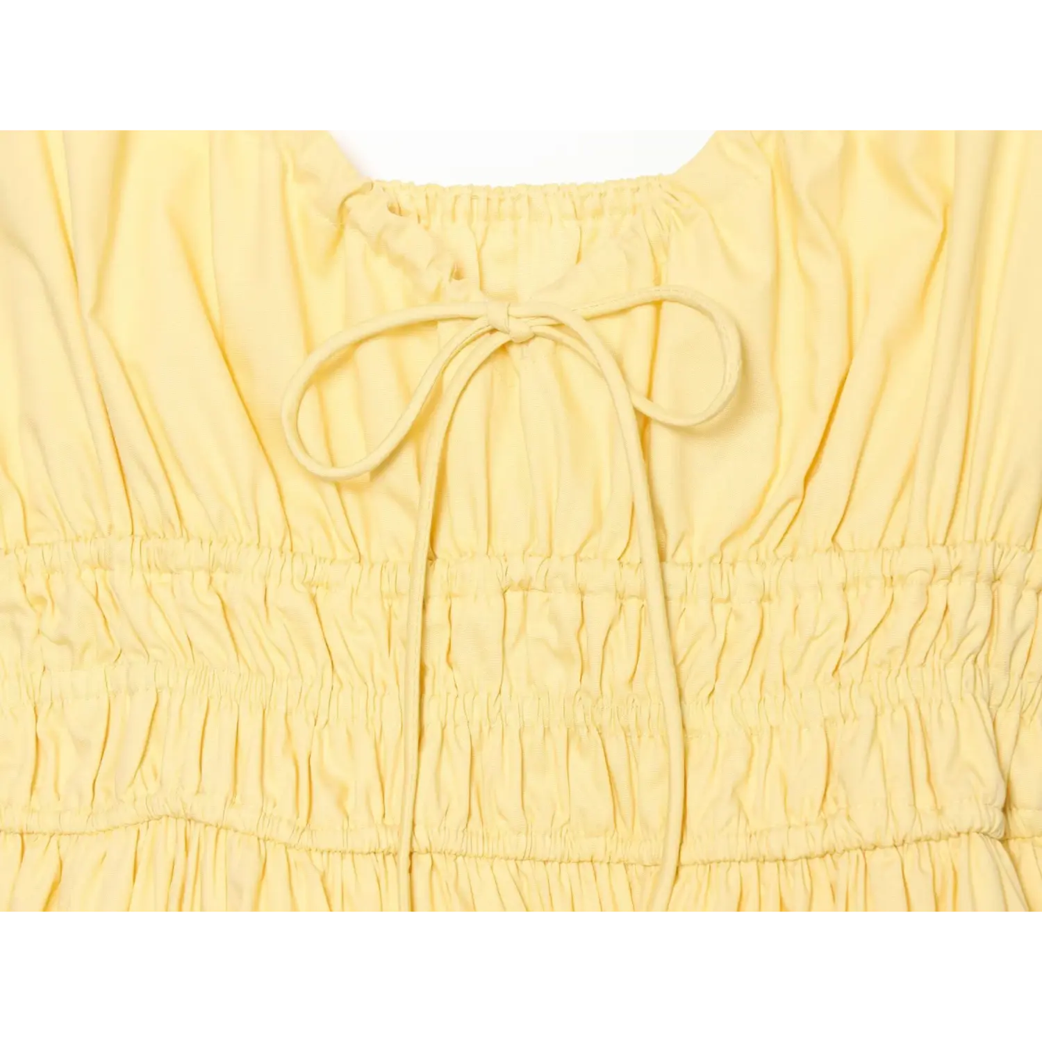 Macro detail of yellow dress front bow tie and multi‑layer smocked elastic waistband