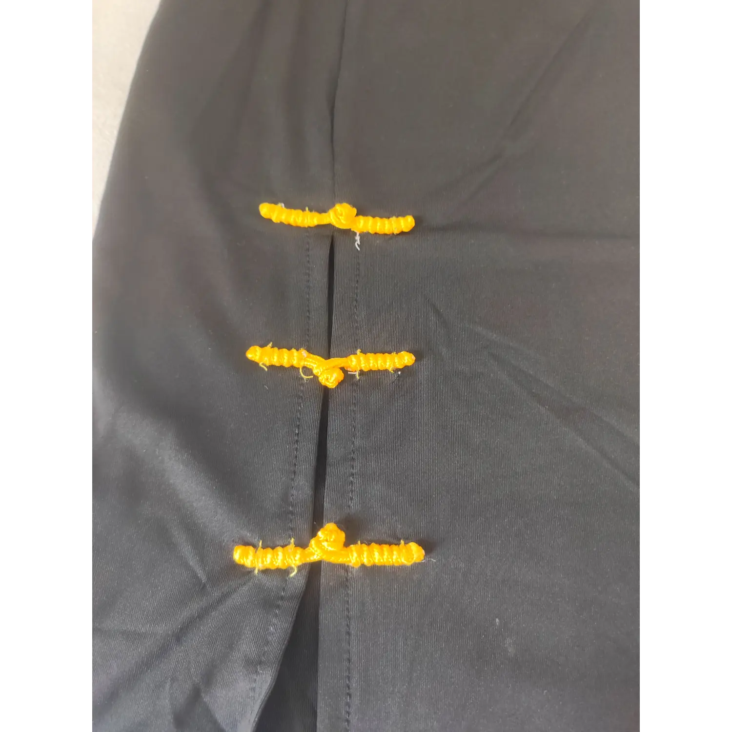 Close up yellow chinese frog knot buttons on side slit of black strapless dress | Detail