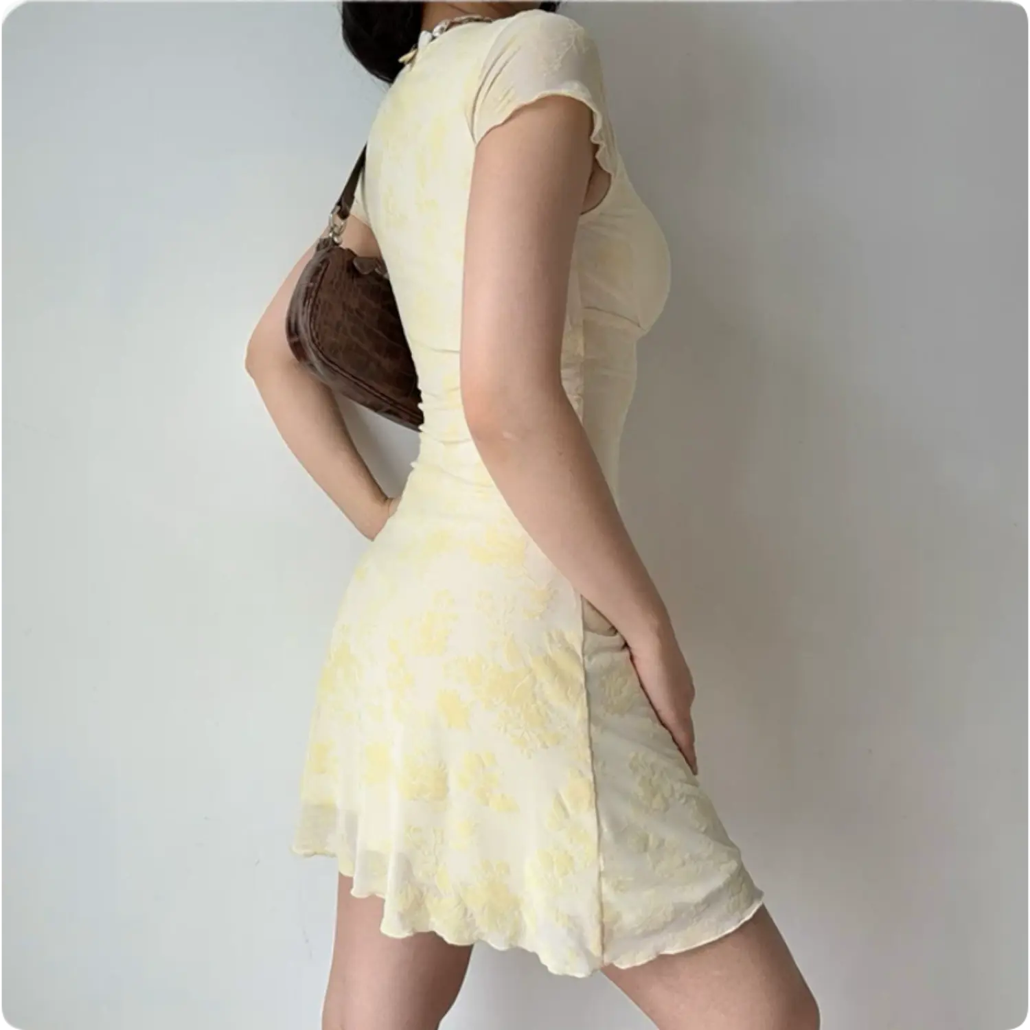Model back three‑quarter view yellow flocked mesh mini dress short ruffle sleeves fitted silhouette flowy hem