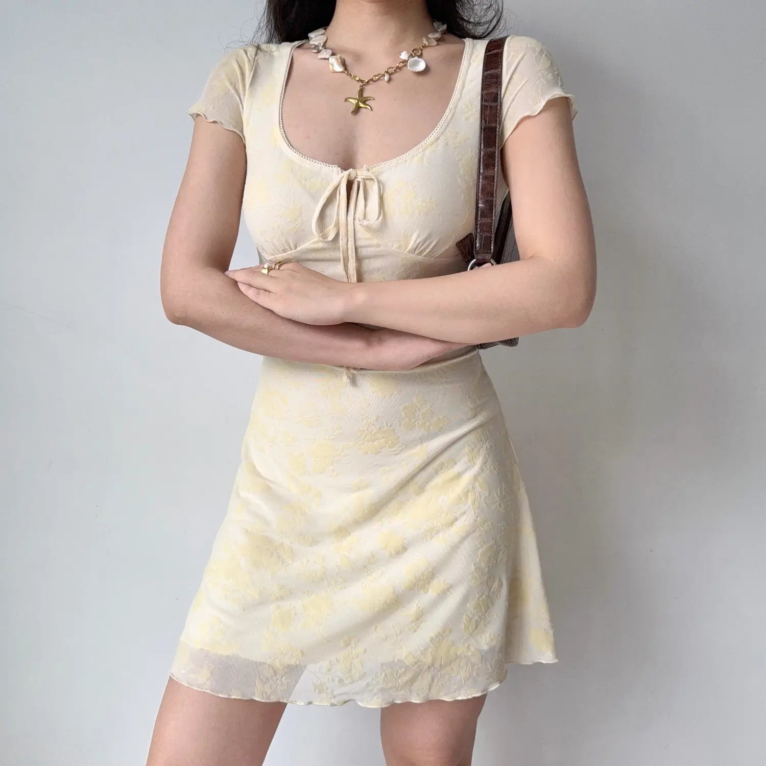 Model front crossed‑arms pose yellow floral flocked mesh mini dress u‑neck front tie short sleeve fitted mini dress