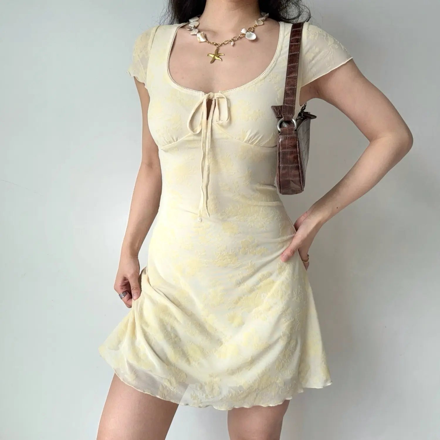 Model front hold‑skirt pose yellow flocked mesh mini dress bodycon fit ruffle sleeve scalloped hem