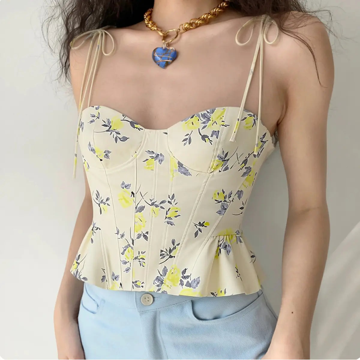 Lifestyle wearing shot of yellow floral print tie-strap peplum corset camisole top, paired with light blue denim jeans