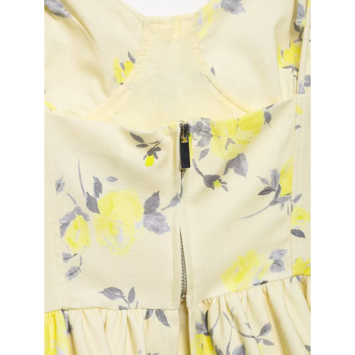 Close-up of the center back zipper pull tab on yellow floral print camisole top