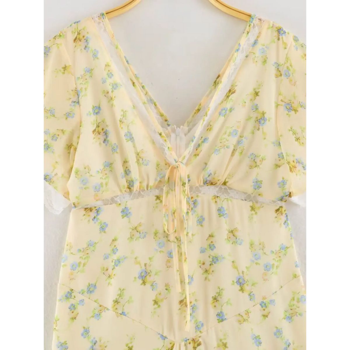 Close up shot of the dress chest part, yellow floral chiffon fabric, deep v neck edged with white lace, front tie and hidden zipper