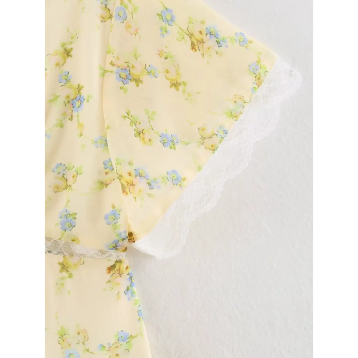 Detail view of short flutter sleeve, yellow floral chiffon with white lace hem
