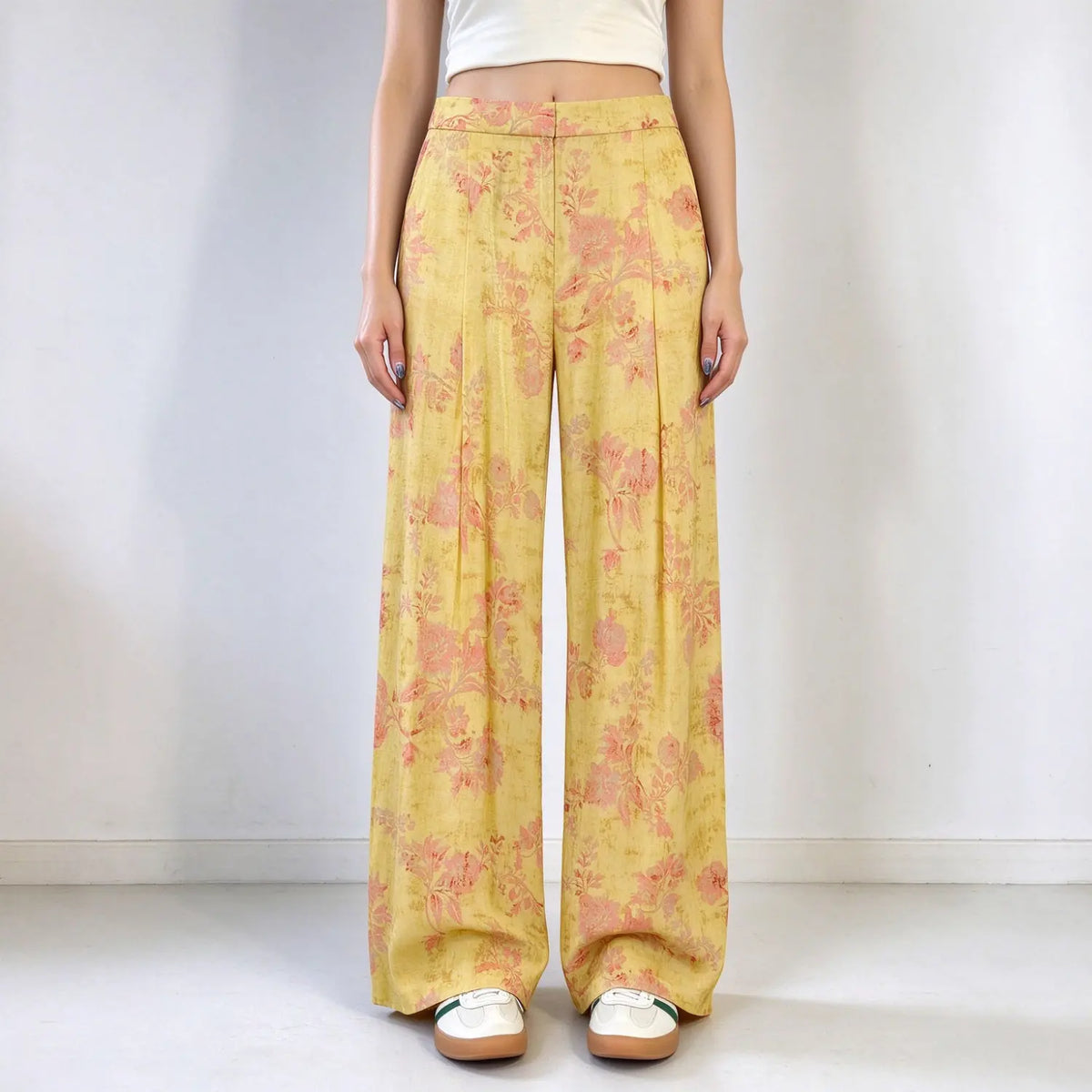 Model wearing yellow floral print wide leg trousers, high waist, front pleats, relaxed flowy silhouette, paired with white cropped top, plain white background
