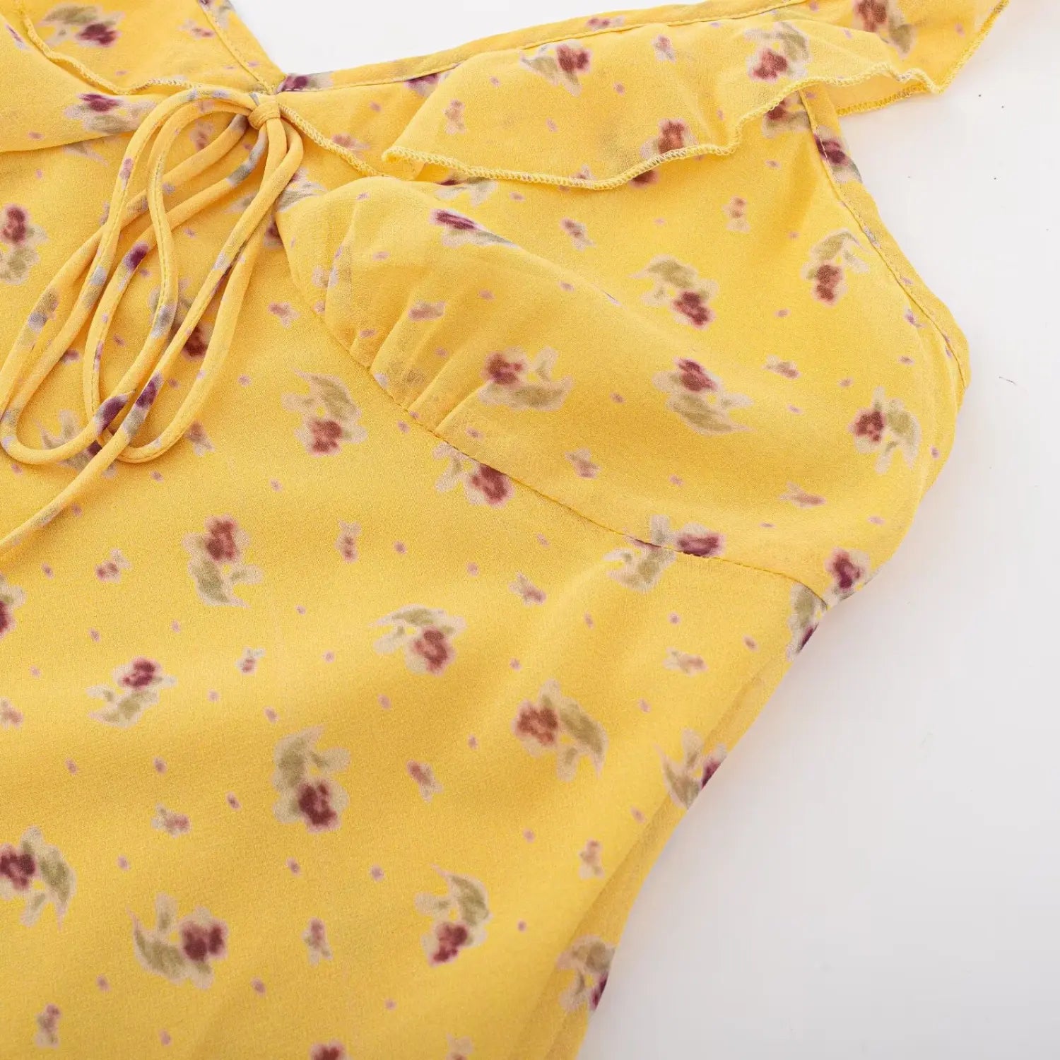 Top down closeup view of yellow floral ruffle cami dress, showcasing v-neck front tie and ruffle trim