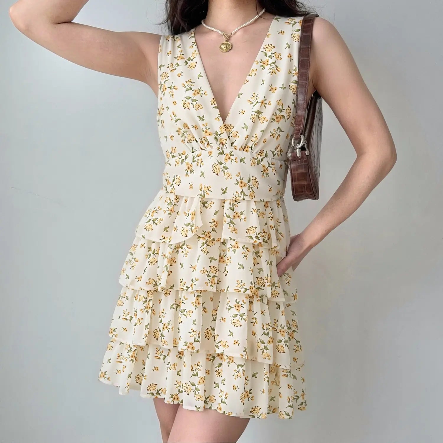 Model wearing cream sleeveless deep v neck yellow floral tiered ruffle mini dress