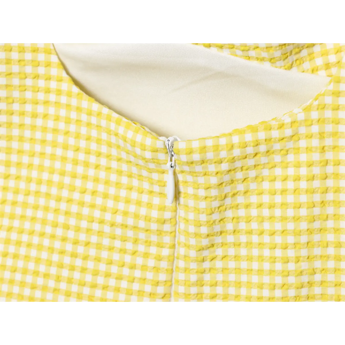 Close-up of the back zipper on the yellow gingham dress, showing the white zipper pull and fabric finish