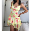 Woman wearing a yellow mesh mini dress with pink hibiscus flowers and white polka dots, posed with both hands relaxed to show the dress's full front design.