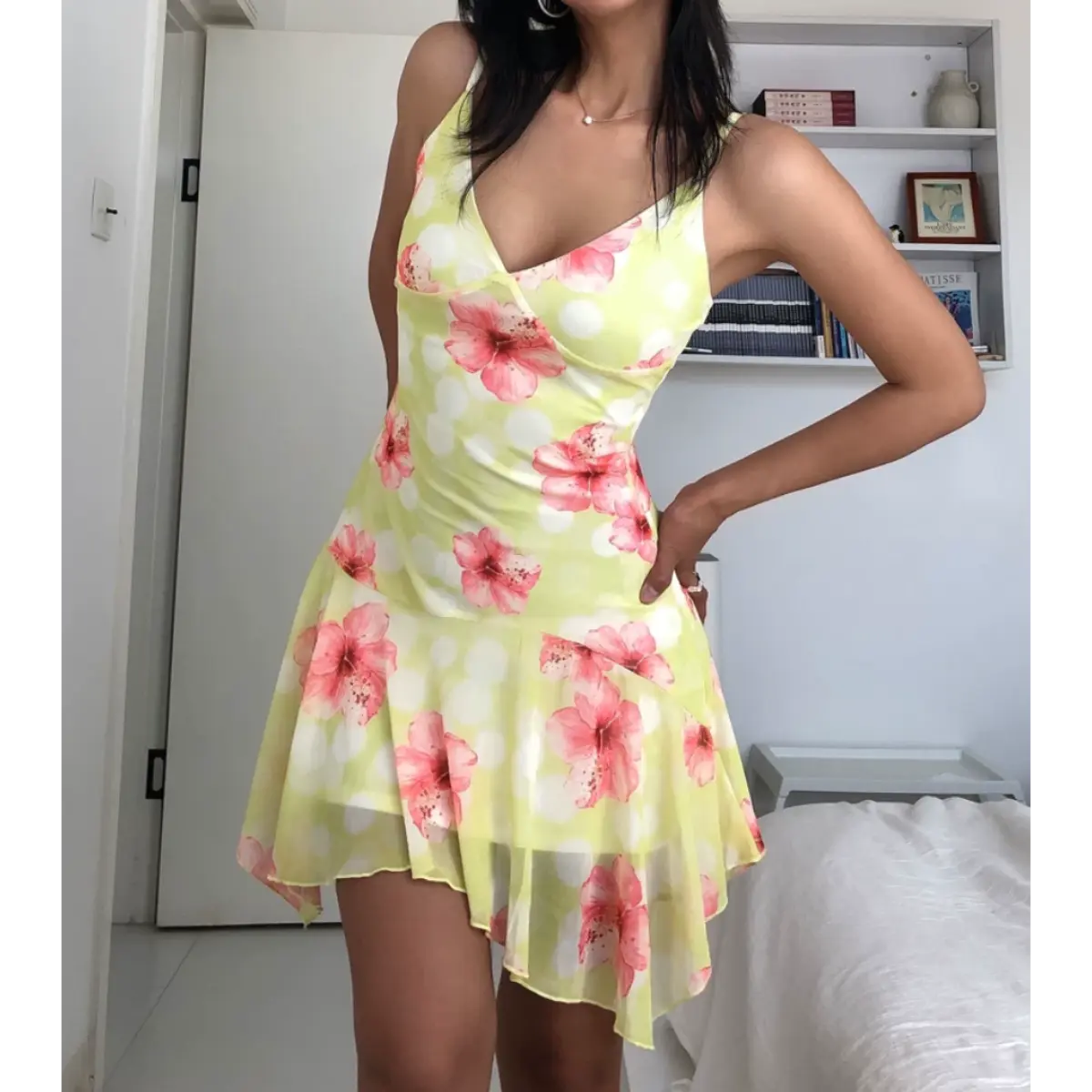 Woman wearing a yellow mesh mini dress with pink hibiscus flowers and white polka dots, posed with both hands relaxed to show the dress's full front design.