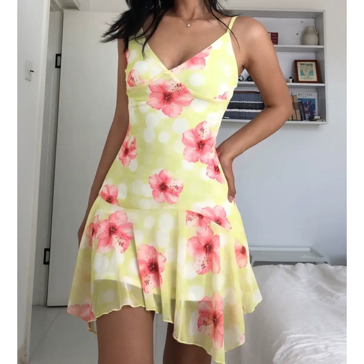 Woman wearing a yellow mesh mini dress with pink hibiscus flowers and white polka dots, posed with both hands relaxed to show the dress's full front design.