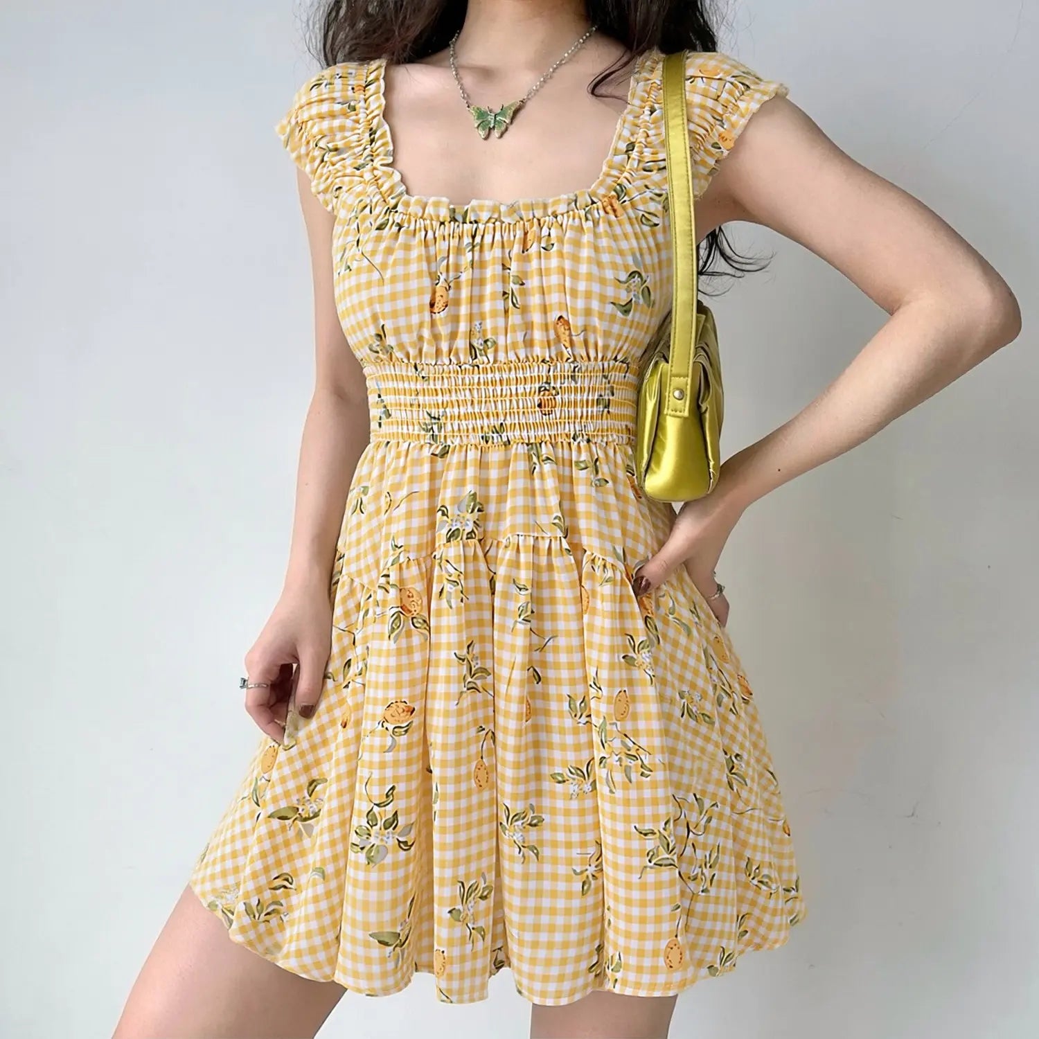 female model wearing yellow white gingham lemon print tiered mini sundress square ruffle neck smocked waist summer outfit lifestyle shot
