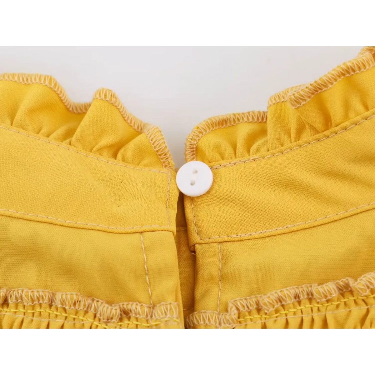 Close-up of panel seam with white round button on ruffle trimmed yellow fabric