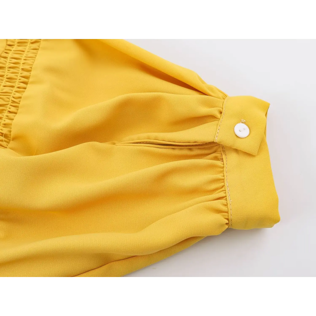 Close-up of gathered elastic cuff with white button on yellow puff sleeve