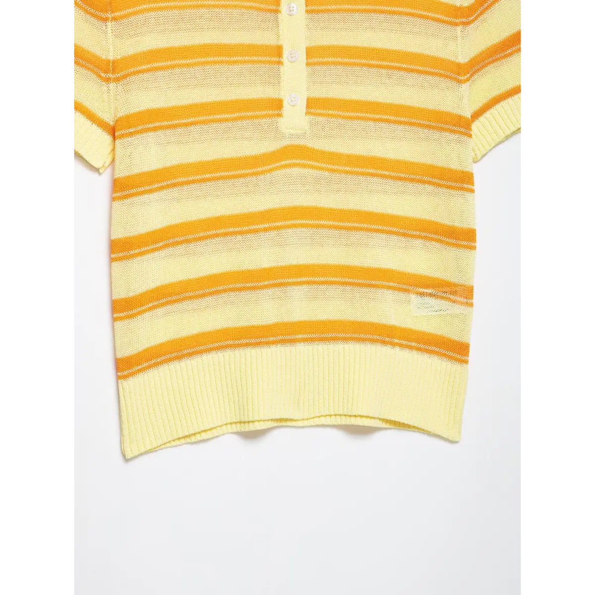 Close-up detail of the ribbed bottom hem and striped pattern on a yellow and orange knit polo top.