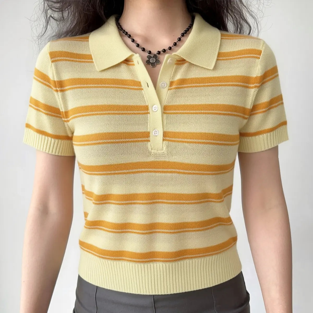 Model wearing a yellow and orange striped knit polo top with a collared neckline, four-button placket, and ribbed hem, front view.