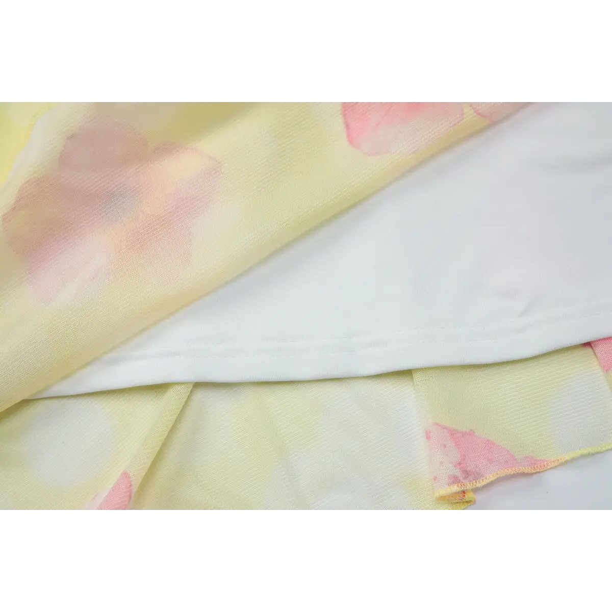 Close-up view of the inner lining of a yellow mesh dress with pink hibiscus print, showing the stitching and contrast between sheer outer layer and opaque lining.