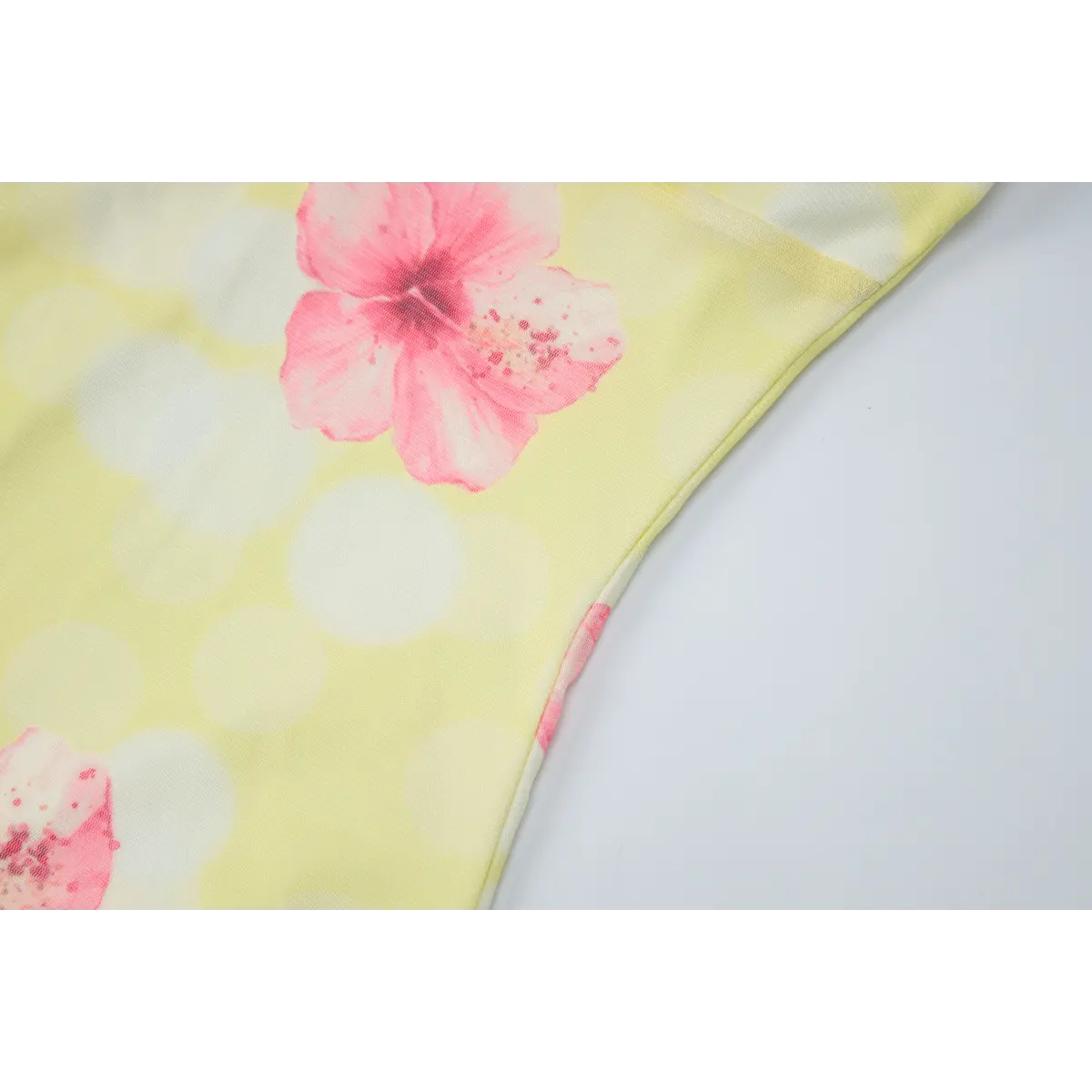 Close-up view of the side seam of a yellow mesh dress with pink hibiscus print, showing the clean stitching and print placement.
