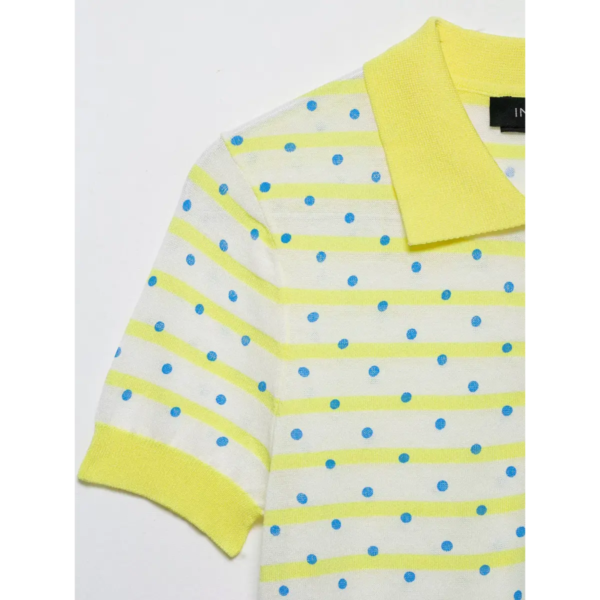 Close-up of the collar and sleeve of a yellow and white polka dot knit polo shirt, showing the ribbed yellow trim and the striped and dotted knit pattern.