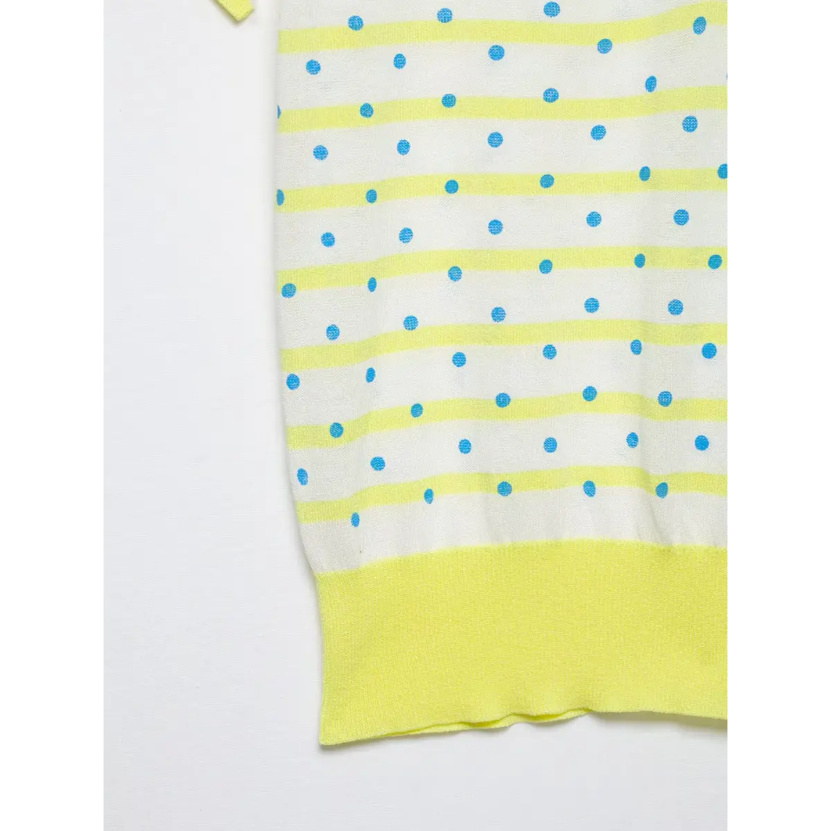 Close-up of the hem and fabric of a yellow and white polka dot knit polo shirt, highlighting the ribbed yellow bottom band and textured knit pattern.