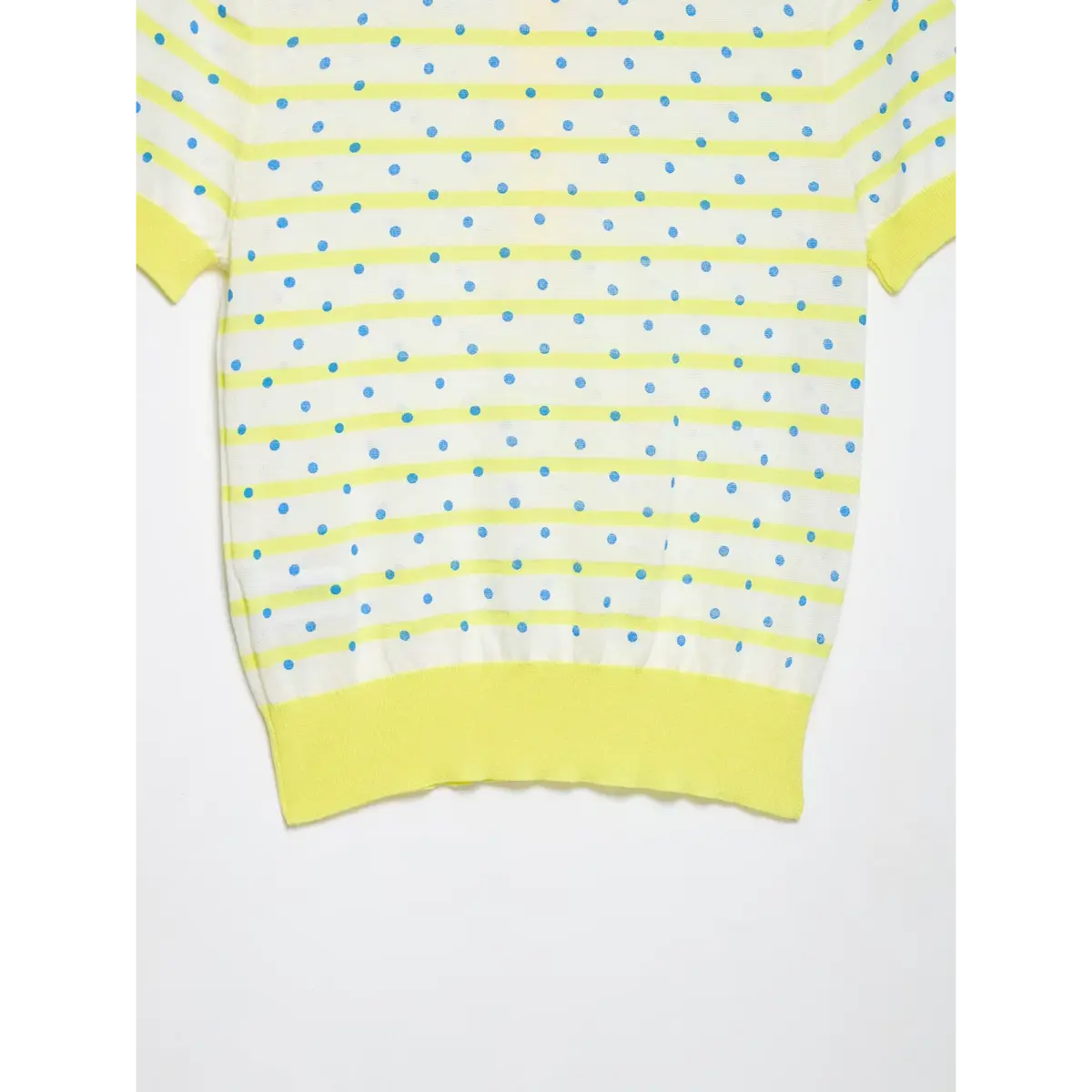 Close-up of the side and hem of a yellow and white polka dot knit polo shirt, showing the striped and dotted pattern and ribbed yellow bottom band.
