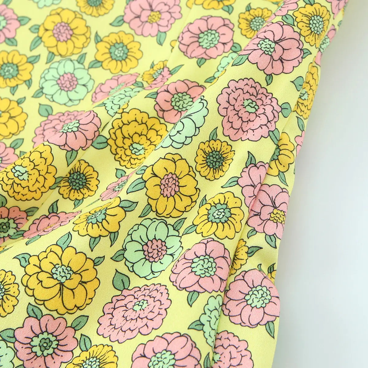 Close-up of the fabric texture on the yellow halter top, showing the smooth woven material and detailed retro floral print