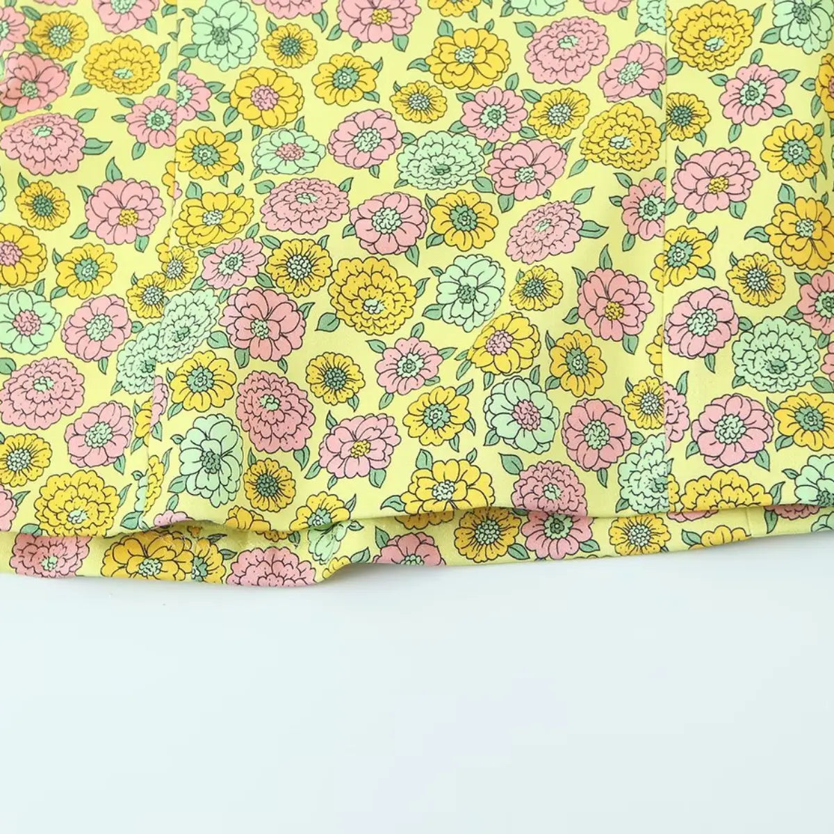 Hem view of the yellow retro floral halter top, showing the straight hem and repeating 1960s-style floral pattern