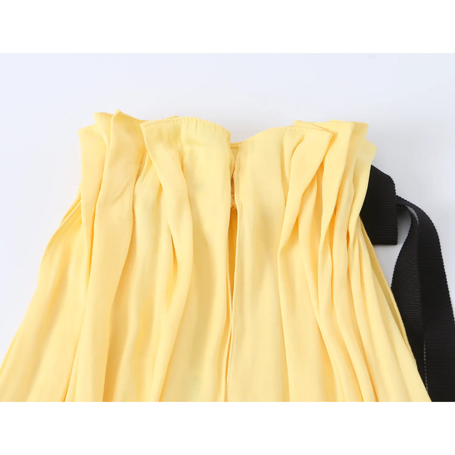 Close-up of front halter neck, elasticated ruffle shirring, central vertical seam, loose draped lightweight yellow fabric, side black grosgrain ribbon tie partial view