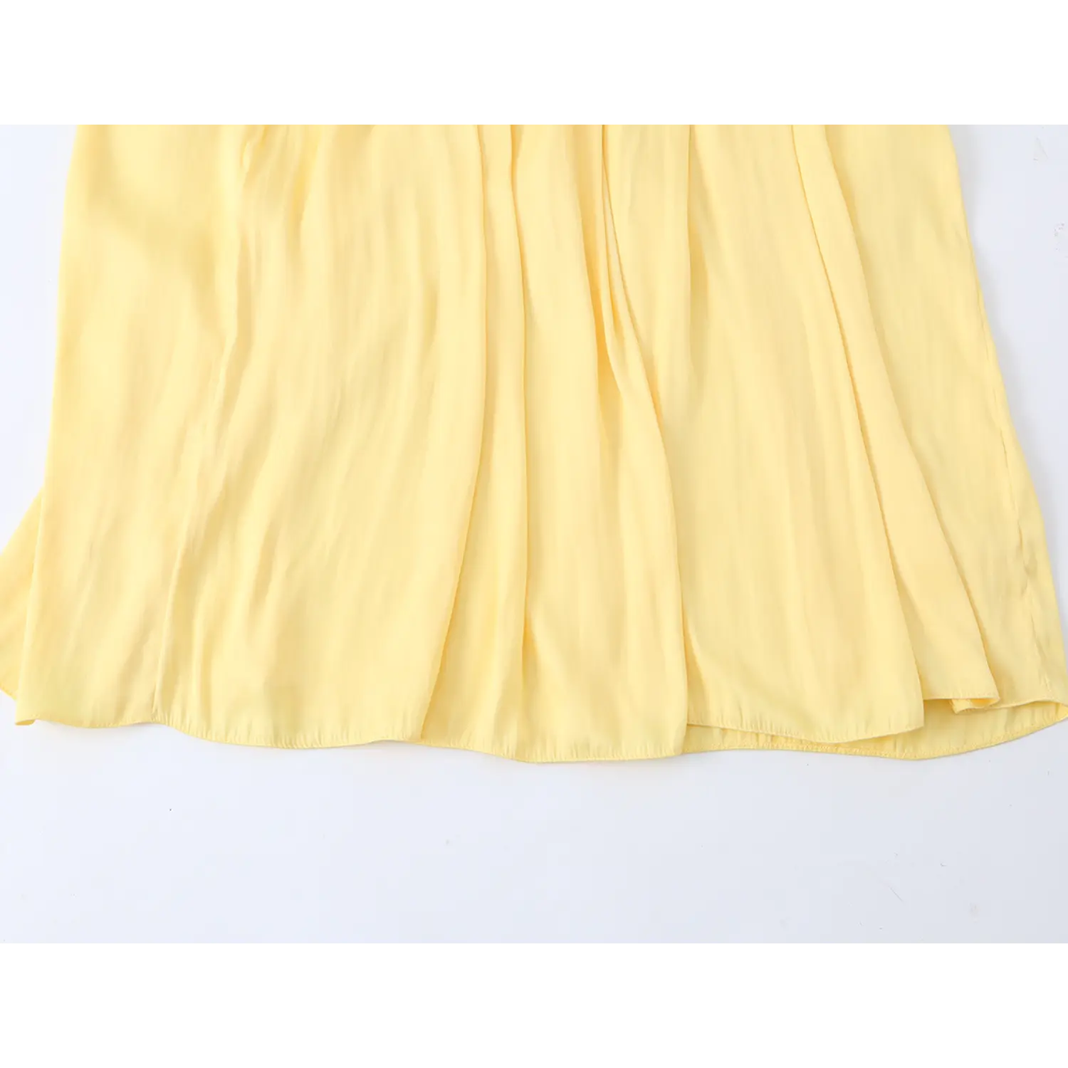 Flat shot of full skirt hem, multiple soft vertical fabric folds, neat fine lockstitch bottom edge, lightweight wrinkle-resistant yellow woven fabric