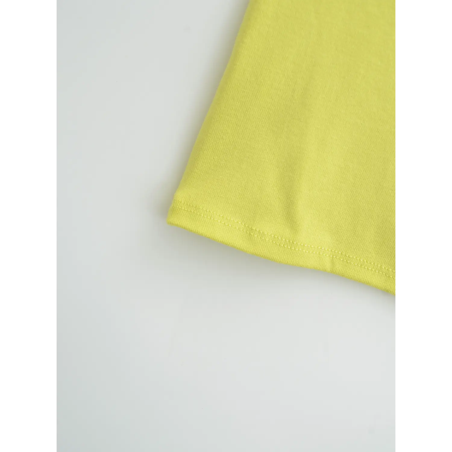 Yellow spaghetti strap tank bottom hem flat close-up, even straight double line overlock soft stretch rib knit neat edge binding white background shot