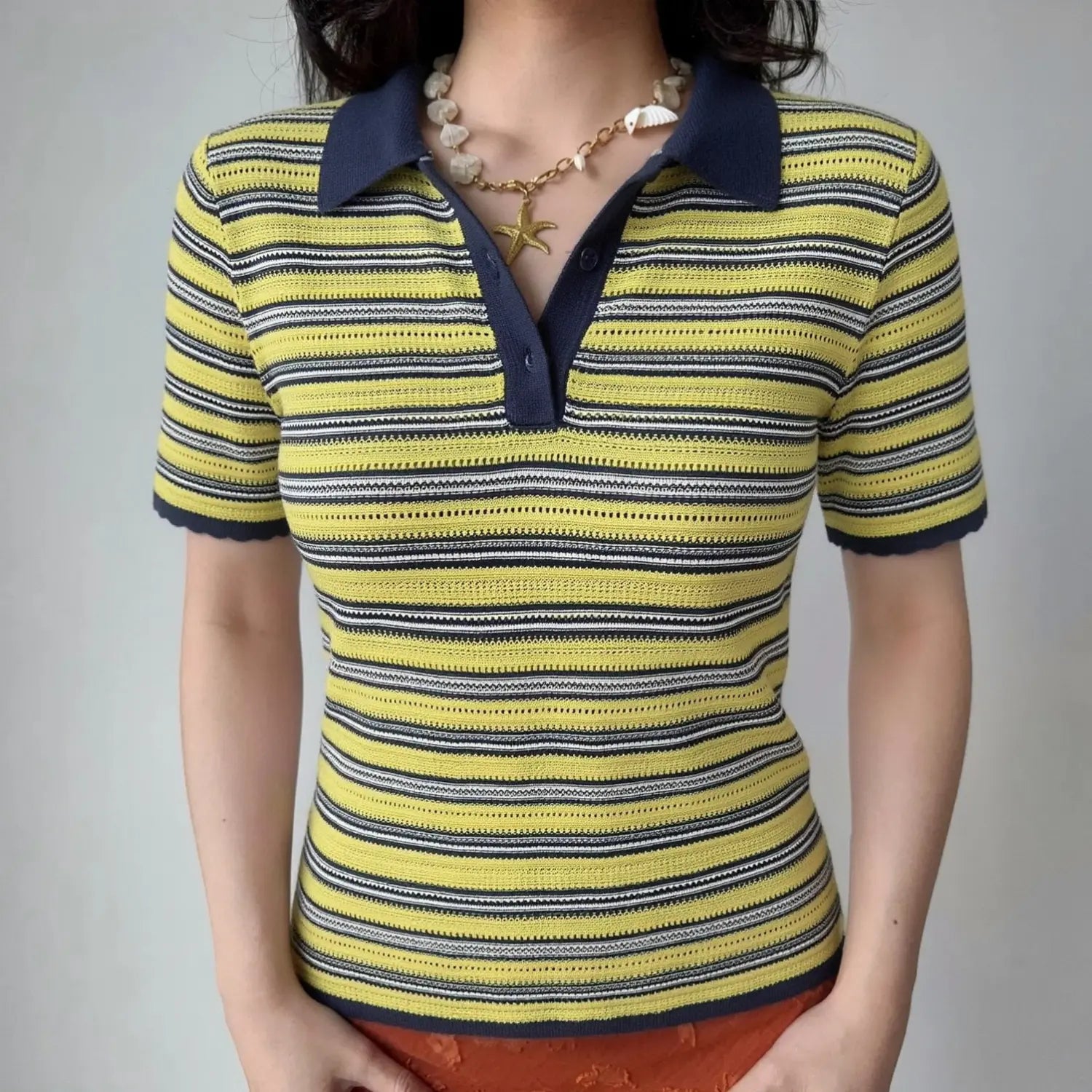 Front lifestyle shot on model, contrast navy polo collar, three-button placket, yellow navy white striped openwork knit short sleeve top, matched with shell starfish necklace and orange bottoms, casual summer outfit